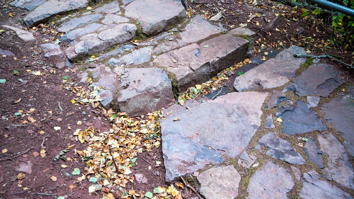 De rødlige steinene i trappen er ringerikssandstein, dannet da sand over tid ble presset sammen og omdannet til stein. Trappen er bygget av lokal stein fra området, og bildet viser også en dreneringsrenne som leder vann bort fra stien.