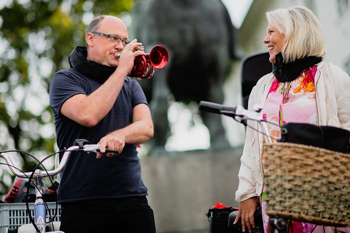 En mann som spiller trompet for en dame på gaten med sykkel