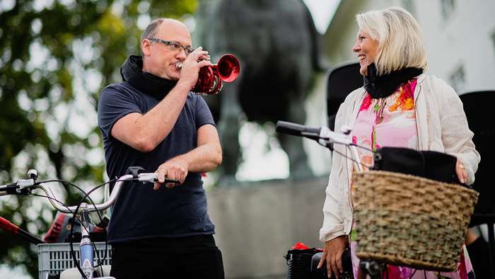 En mann som spiller trompet for en dame på gaten med sykkel